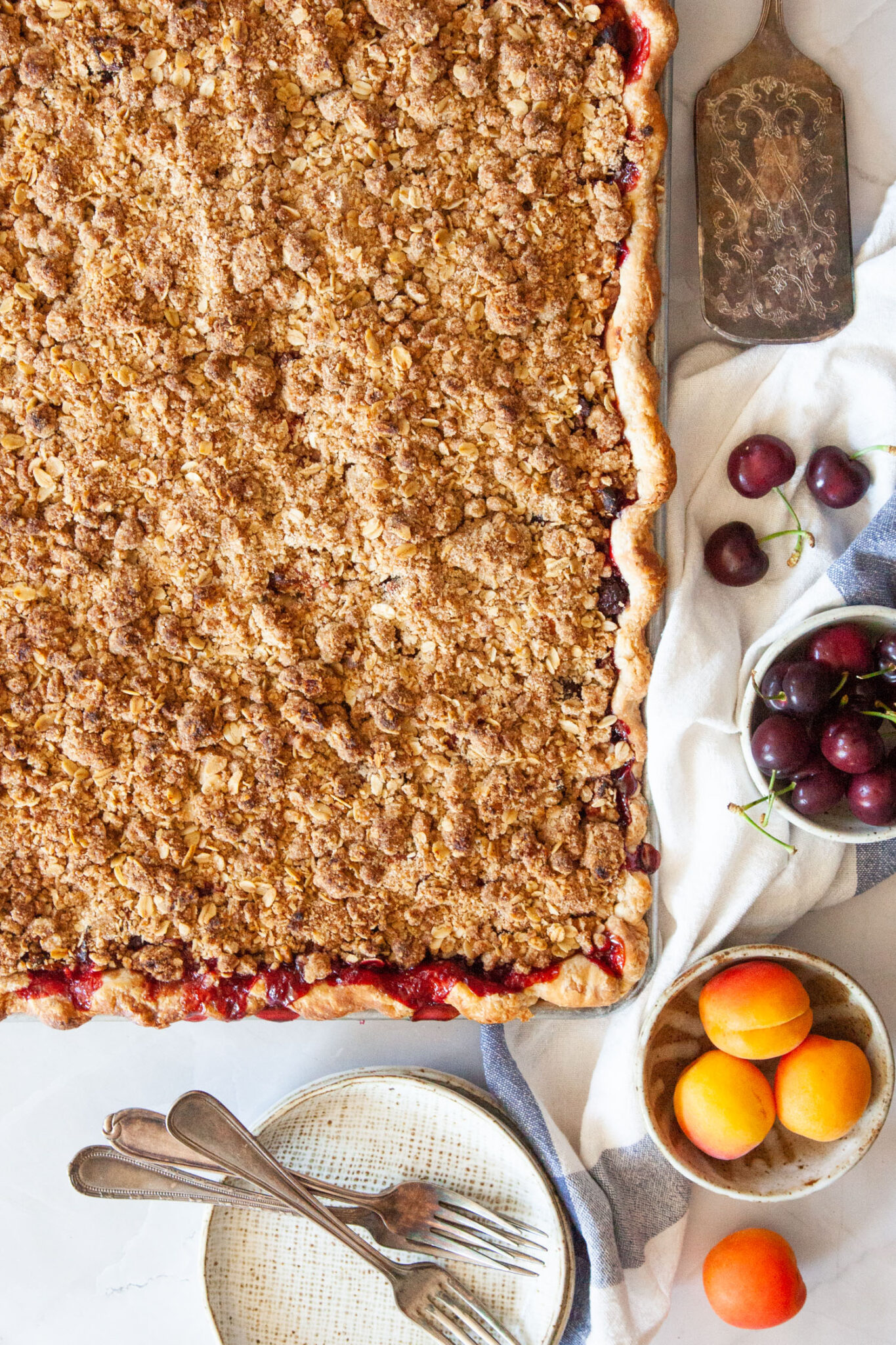 A large apricot and cherry slab pie with plates and fresh apricots and cherries next to it.